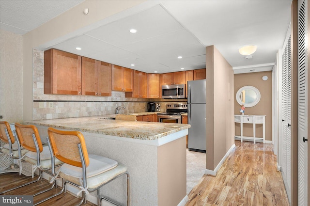 kitchen featuring appliances with stainless steel finishes, a kitchen bar, kitchen peninsula, and light wood-type flooring