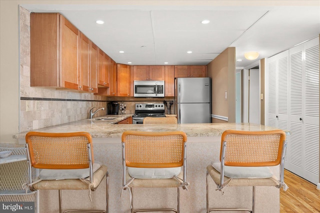 kitchen featuring a breakfast bar, sink, light hardwood / wood-style flooring, kitchen peninsula, and stainless steel appliances