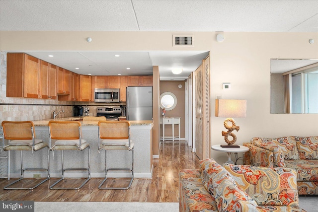 kitchen featuring sink, a kitchen breakfast bar, kitchen peninsula, stainless steel appliances, and light wood-type flooring