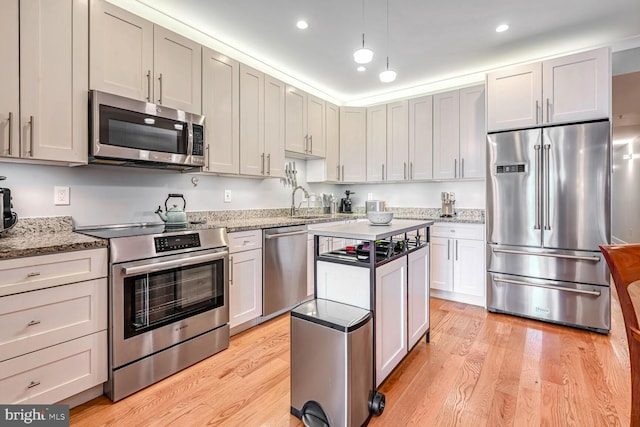 kitchen with appliances with stainless steel finishes, light wood-type flooring, and light stone counters