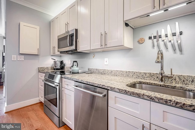 kitchen with appliances with stainless steel finishes, white cabinetry, sink, light stone counters, and light hardwood / wood-style flooring