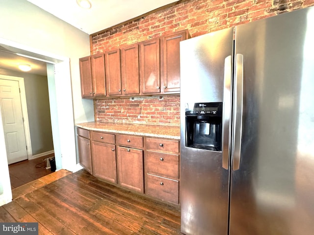 kitchen featuring dark hardwood / wood-style floors, brick wall, stainless steel fridge, and light stone countertops