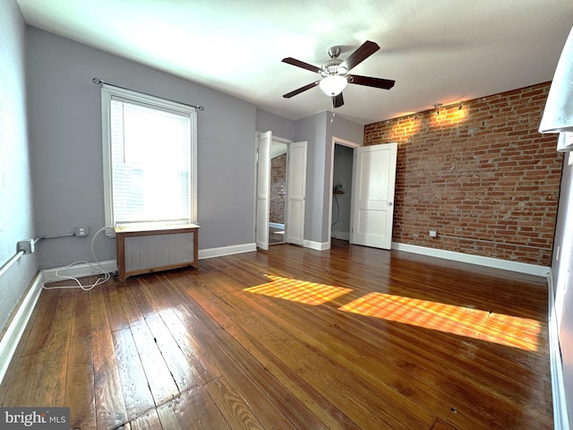 empty room featuring ceiling fan, brick wall, dark hardwood / wood-style floors, and radiator