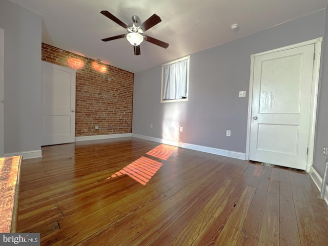 unfurnished living room with ceiling fan, brick wall, and wood-type flooring