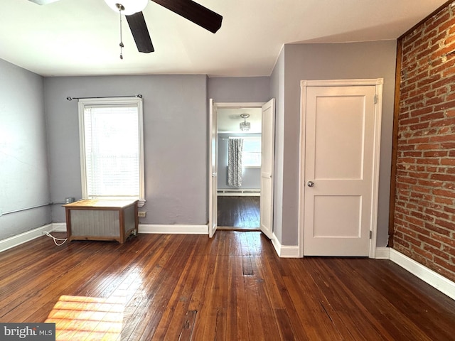 empty room with dark wood-type flooring, brick wall, radiator heating unit, and ceiling fan