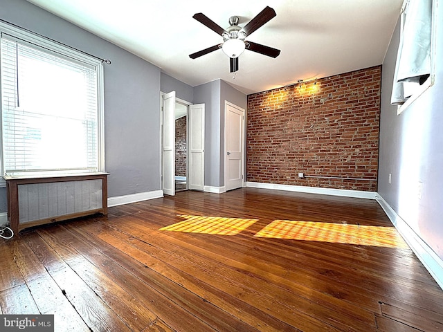 unfurnished bedroom with ceiling fan, brick wall, radiator heating unit, and dark hardwood / wood-style flooring