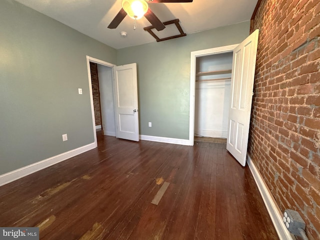 unfurnished bedroom with ceiling fan, brick wall, dark hardwood / wood-style floors, and a closet