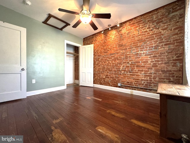 unfurnished bedroom featuring ceiling fan, brick wall, dark hardwood / wood-style flooring, and a closet