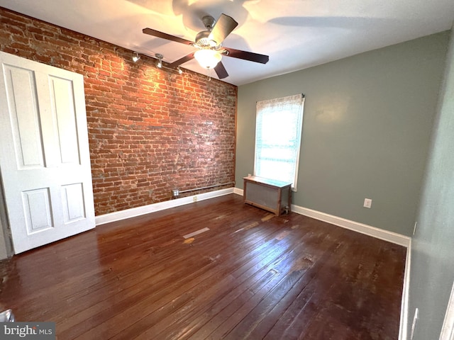 spare room with dark wood-type flooring, ceiling fan, brick wall, and rail lighting