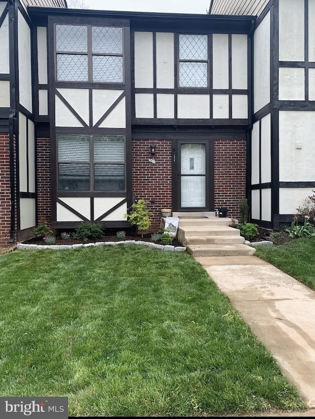 view of exterior entry with a yard, brick siding, and stucco siding