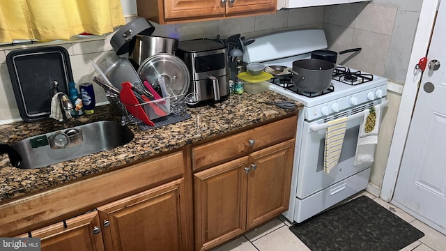 kitchen with tasteful backsplash, sink, white range with gas stovetop, and dark stone countertops