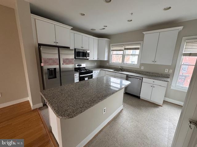 kitchen featuring a kitchen island, appliances with stainless steel finishes, white cabinets, and dark stone counters