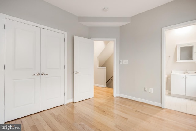 unfurnished bedroom featuring ensuite bath, light hardwood / wood-style flooring, and a closet