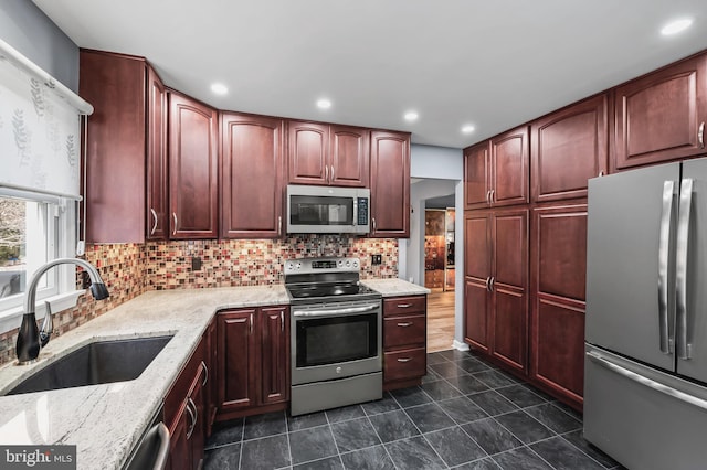 kitchen with sink, appliances with stainless steel finishes, backsplash, light stone counters, and dark tile patterned flooring