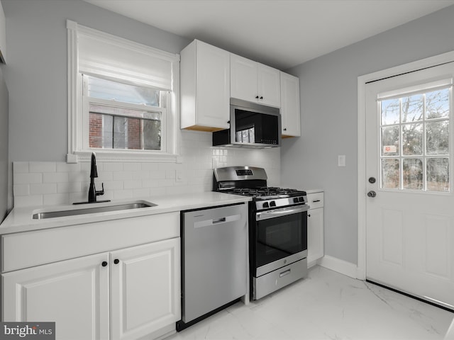 kitchen with stainless steel appliances, a sink, white cabinetry, light countertops, and decorative backsplash