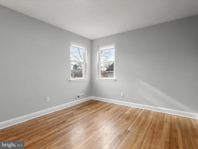 empty room featuring light wood-type flooring, visible vents, and baseboards