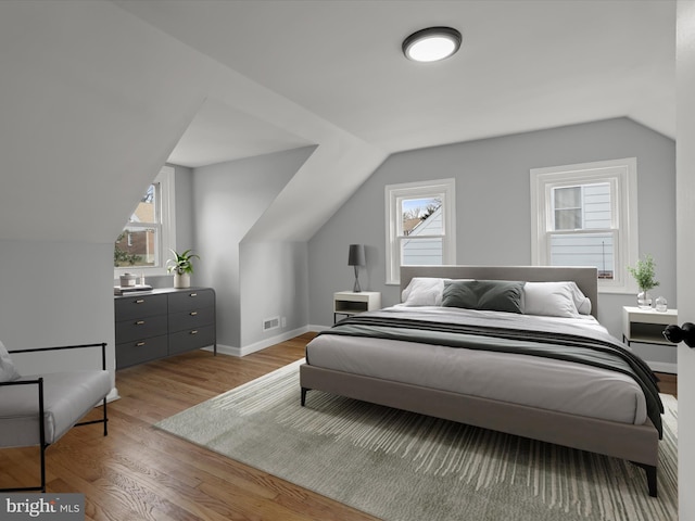 bedroom with light wood-type flooring, visible vents, lofted ceiling, and baseboards