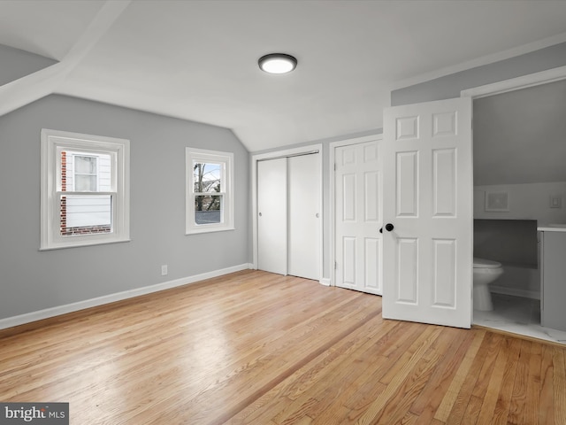 unfurnished bedroom featuring connected bathroom, baseboards, vaulted ceiling, multiple closets, and light wood-type flooring