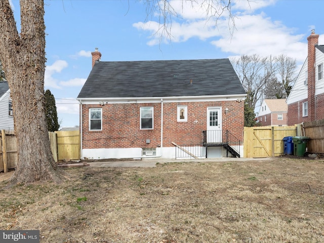 rear view of property with a gate, a chimney, fence, and brick siding