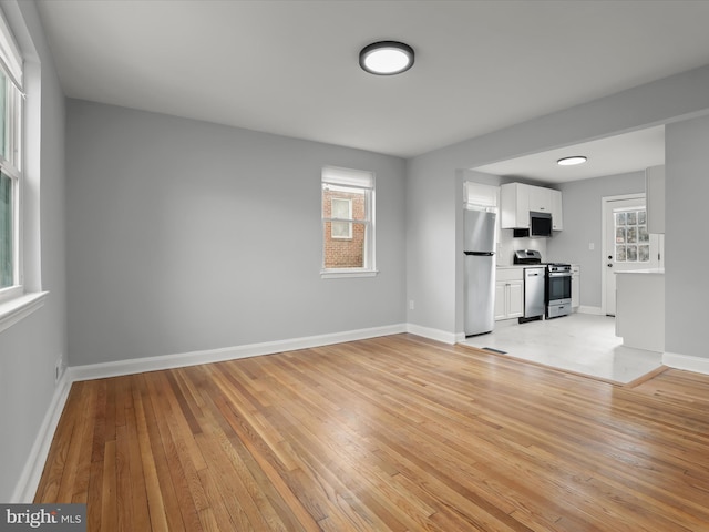 unfurnished living room with light wood-type flooring and baseboards