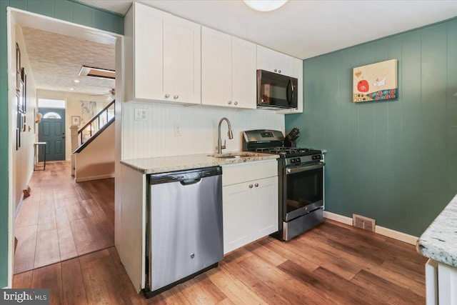 kitchen with sink, white cabinets, light stone counters, light hardwood / wood-style floors, and stainless steel appliances