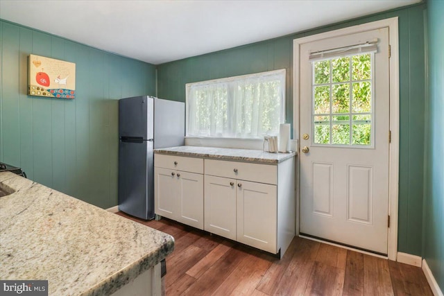 kitchen featuring white cabinetry, stainless steel fridge, dark hardwood / wood-style flooring, and light stone counters