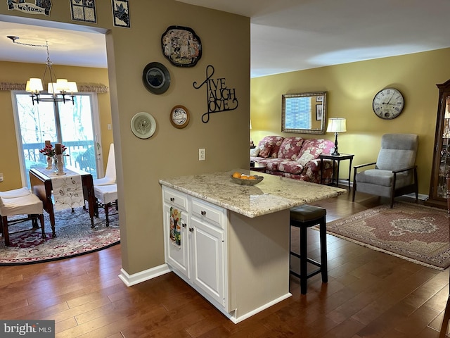 kitchen featuring white cabinetry, hanging light fixtures, light stone countertops, dark hardwood / wood-style flooring, and a chandelier