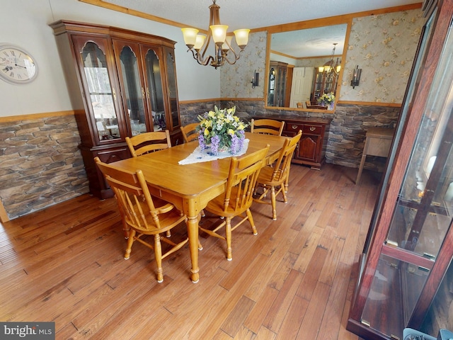 dining space featuring a notable chandelier, ornamental molding, wainscoting, light wood finished floors, and wallpapered walls