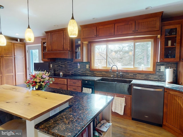 kitchen featuring hanging light fixtures, light wood-style flooring, brown cabinetry, a sink, and dishwasher