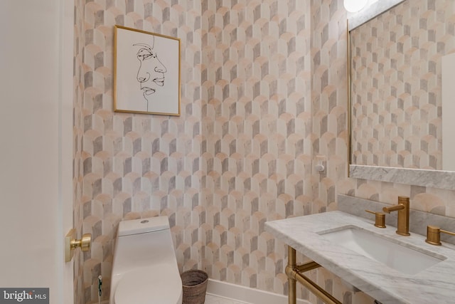 bathroom with toilet, wallpapered walls, baseboards, and vanity