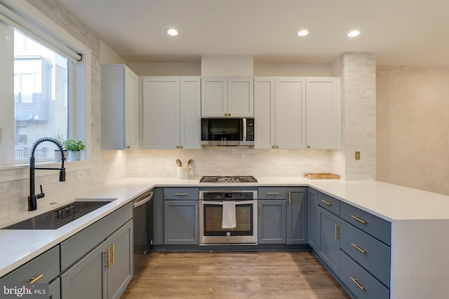 kitchen with light countertops, appliances with stainless steel finishes, a sink, wood finished floors, and a peninsula