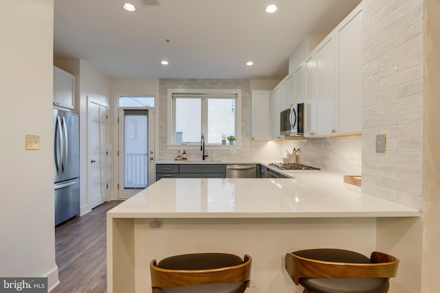 kitchen featuring tasteful backsplash, appliances with stainless steel finishes, a peninsula, a sink, and recessed lighting