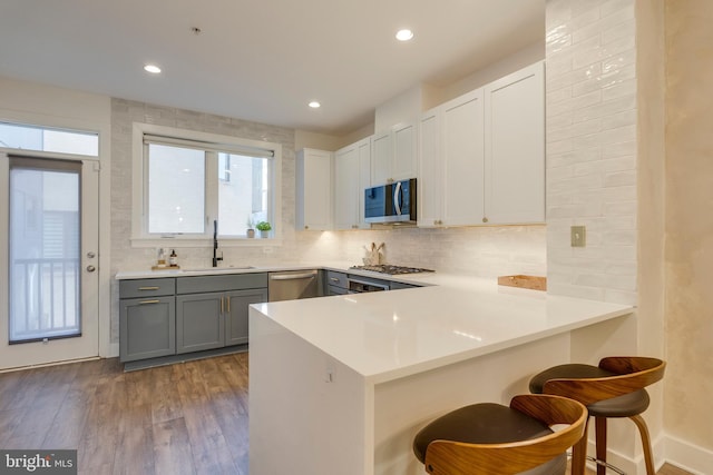 kitchen featuring wood finished floors, a sink, appliances with stainless steel finishes, gray cabinets, and a kitchen bar