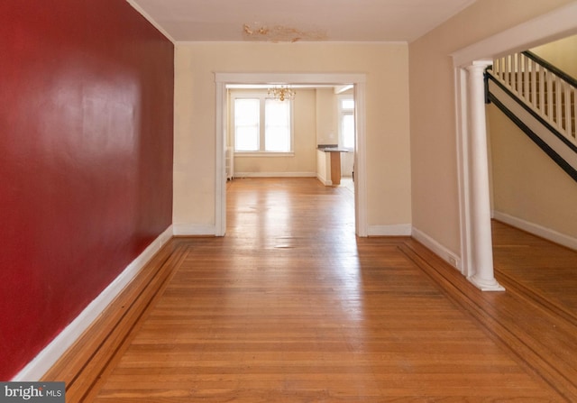 hall featuring ornate columns, a chandelier, and light wood-type flooring