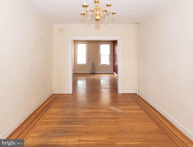 corridor with an inviting chandelier, ornamental molding, radiator heating unit, and wood-type flooring