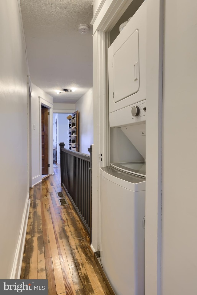 clothes washing area with stacked washer / dryer, dark wood-type flooring, and a textured ceiling