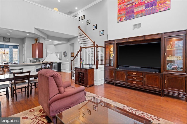 living room with a notable chandelier, wood-type flooring, ornamental molding, and a high ceiling