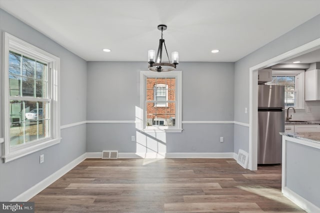 unfurnished dining area with an inviting chandelier, sink, and light hardwood / wood-style flooring