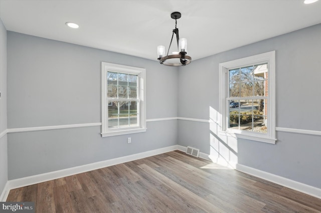 unfurnished dining area with hardwood / wood-style flooring, plenty of natural light, and a notable chandelier