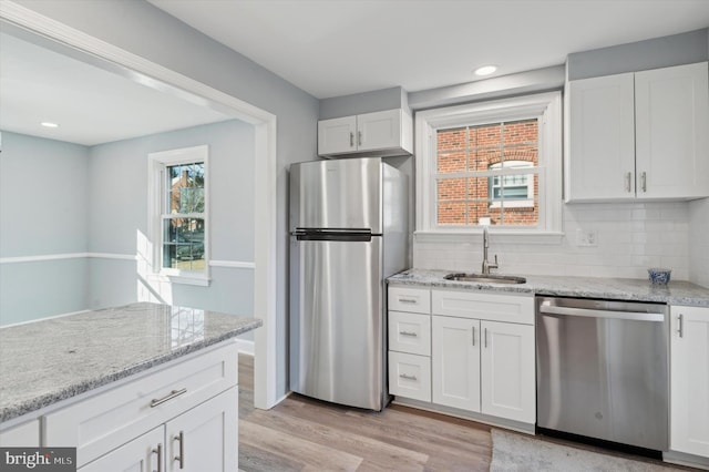 kitchen with appliances with stainless steel finishes, white cabinetry, sink, light stone counters, and light hardwood / wood-style flooring