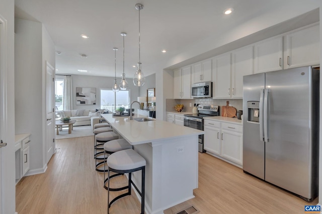 kitchen featuring sink, white cabinetry, decorative light fixtures, a center island with sink, and stainless steel appliances