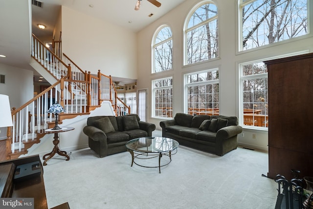 carpeted living area featuring visible vents, a high ceiling, stairway, and a ceiling fan