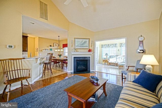 living area featuring visible vents, a fireplace with flush hearth, a ceiling fan, wood finished floors, and high vaulted ceiling