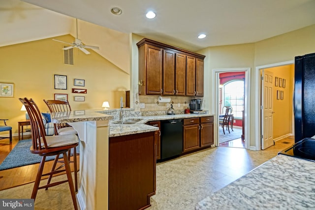 kitchen with a breakfast bar, decorative backsplash, vaulted ceiling, a peninsula, and black appliances