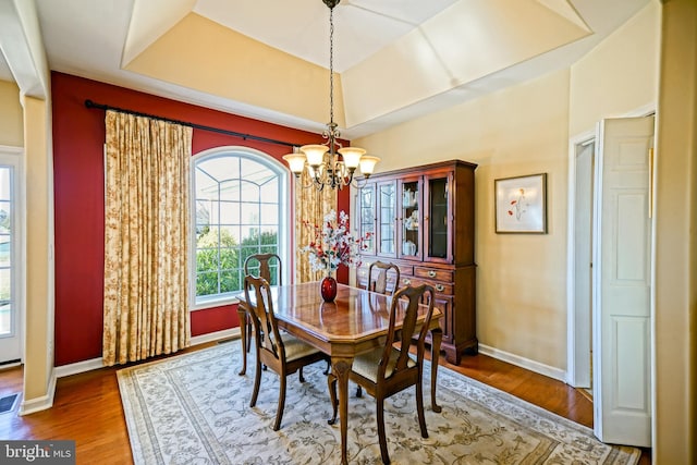 dining space featuring a chandelier, a tray ceiling, wood finished floors, and baseboards