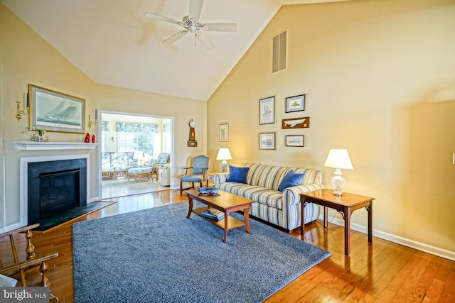 living room with baseboards, visible vents, a glass covered fireplace, hardwood / wood-style flooring, and high vaulted ceiling