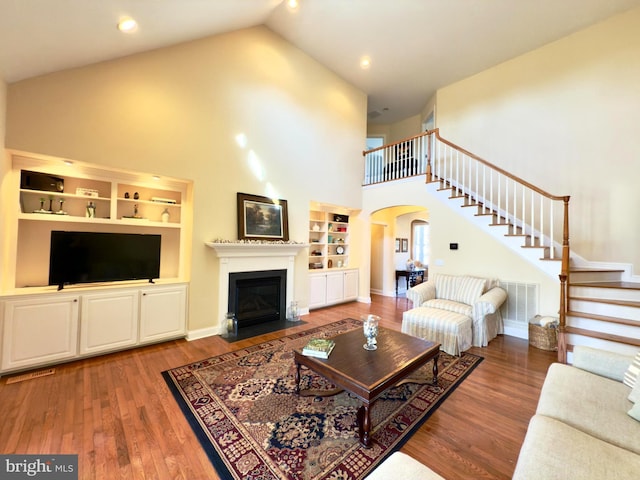 living room with hardwood / wood-style flooring, high vaulted ceiling, and built in shelves