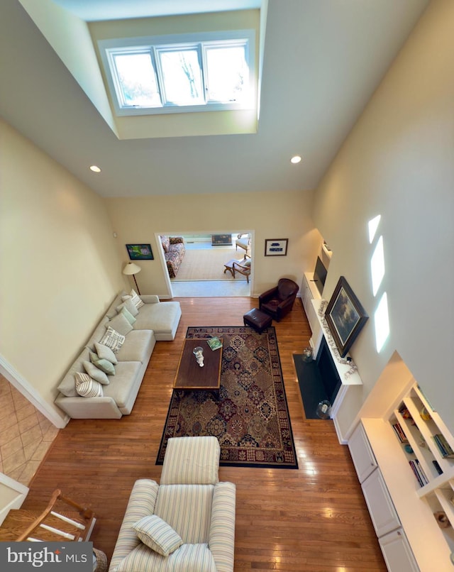 living room featuring a towering ceiling, wood-type flooring, and a skylight