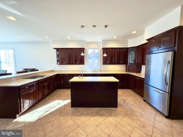 kitchen featuring stainless steel refrigerator, hanging light fixtures, black electric stovetop, an island with sink, and kitchen peninsula