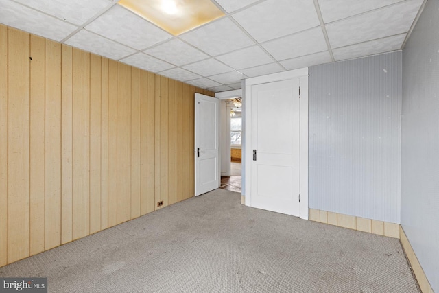 carpeted spare room with wood walls and a drop ceiling